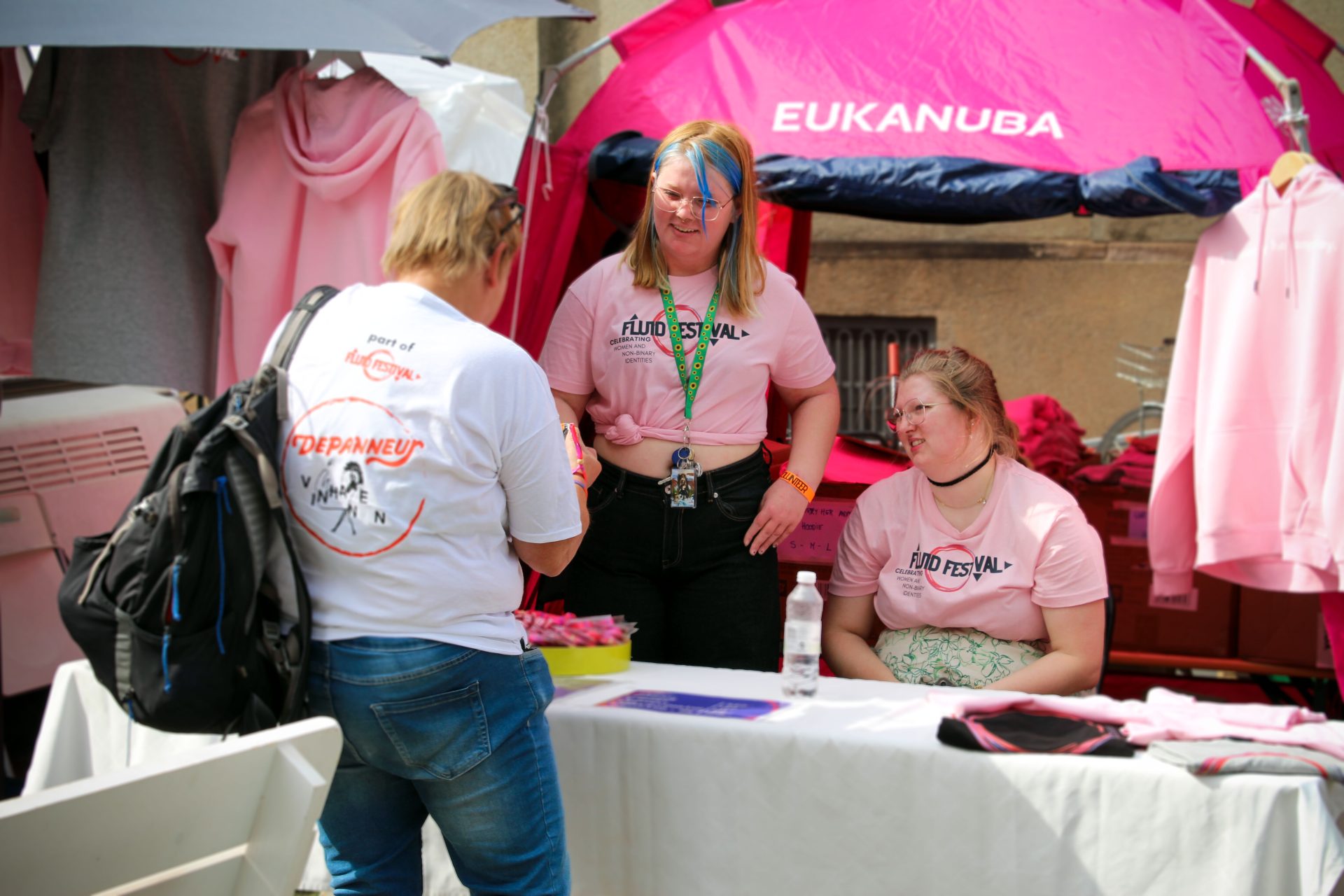 To personer i lyserødt tøj fra Sputnik Stu København, som sælger armbånd til en person på Fluid Festival.